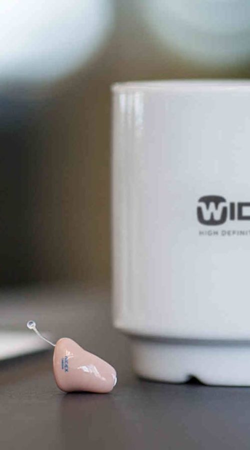 widex-cup-on-table-next-to-a-hearing-aid-1920-1080-1.jpg
